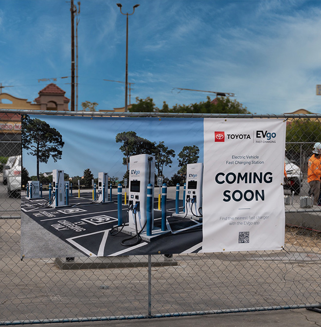 Picture of "coming soon" sign on fence announcing development of fast charging station